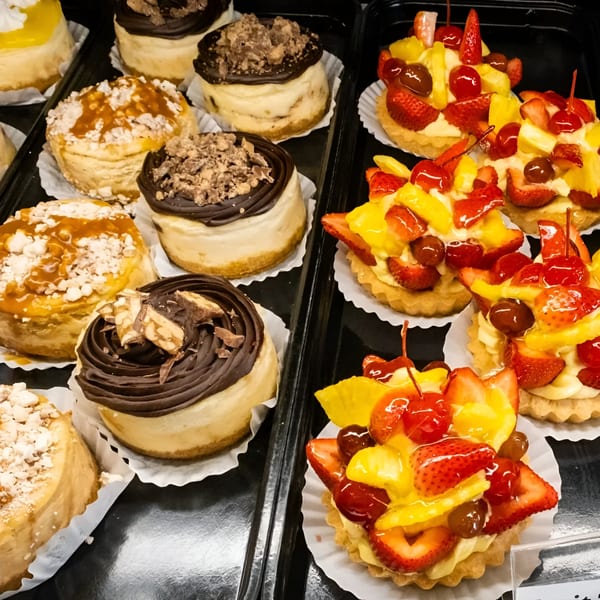 A display of various mini cheesecakes and fruit tarts from Pickles Deli, showcasing dessert options.