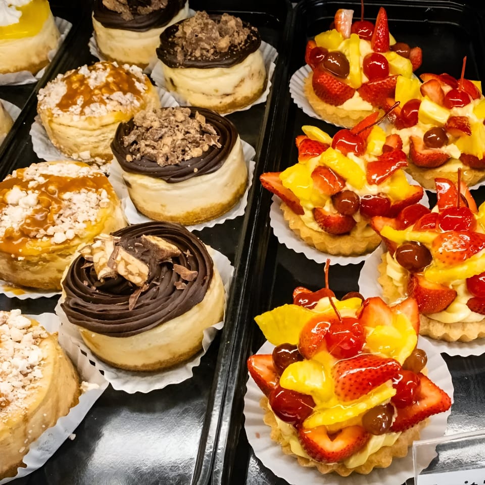 A display of various mini cheesecakes and fruit tarts from Pickles Deli, showcasing dessert options.
