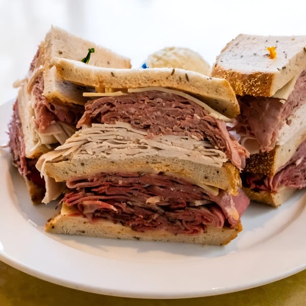 A large deli sandwich with layers of pastrami, turkey, and cheese on rye bread.