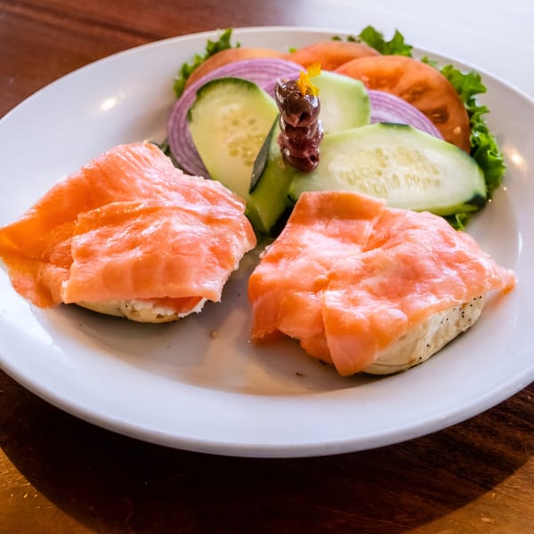 Smoked salmon and cream cheese on two bagel halves, with a side salad of lettuce, tomato, cucumber, and red onion.