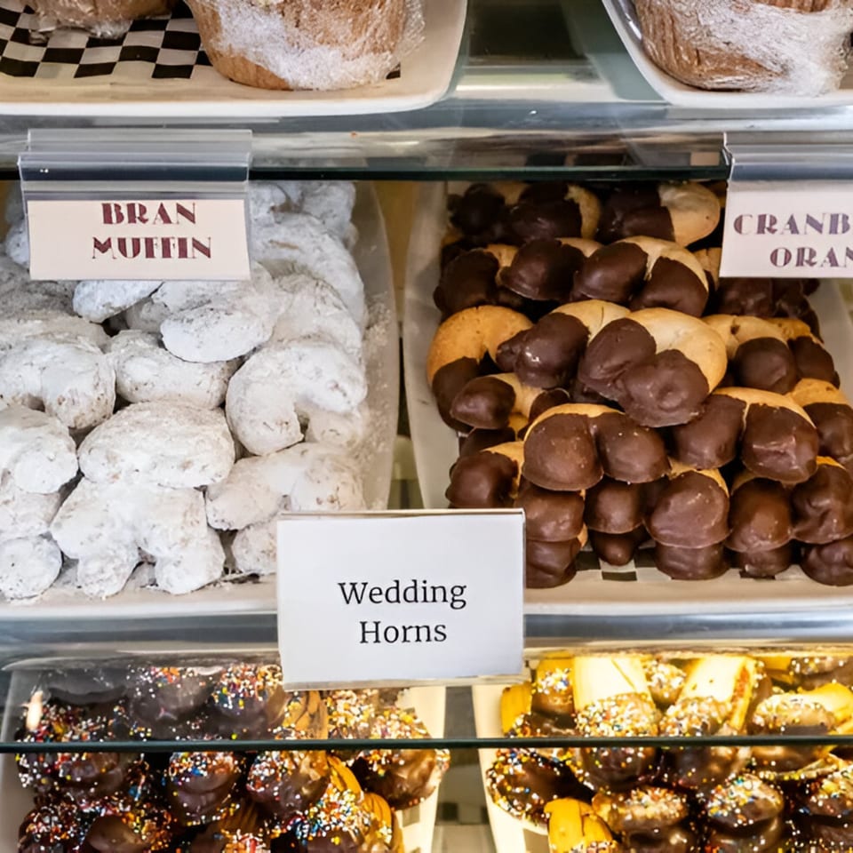 A deli display case filled with powdered sugar cookies, chocolate-dipped pastries, and sprinkle-covered treats.