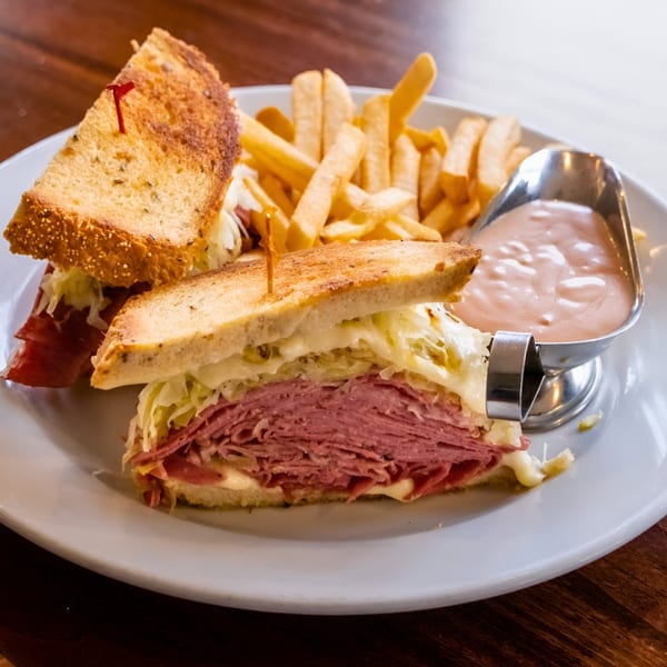 Pickles Deli's Reuben sandwich with corned beef, sauerkraut, melted cheese, and fries with dipping sauce.