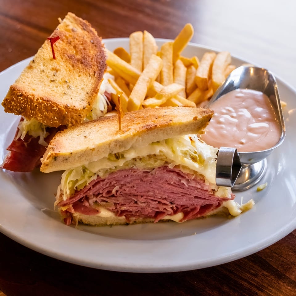 Pickles Deli's Reuben sandwich with corned beef, sauerkraut, melted cheese, and fries with dipping sauce.