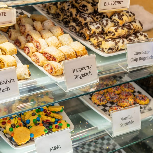 A deli display case filled with various rugelach pastries, M&M cookies, and vanilla sprinkle cookies.