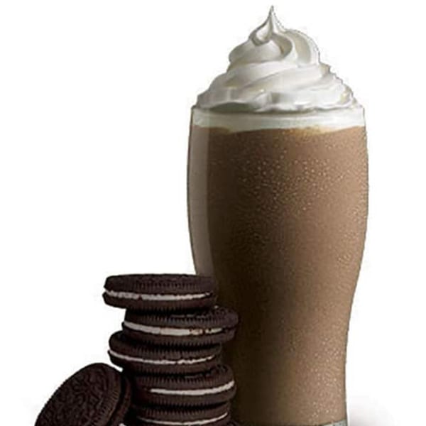 A chocolate milkshake with whipped cream and a stack of Oreo cookies on a white background.