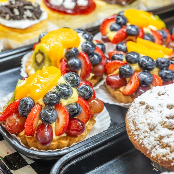 Assortment of fruit tarts with blueberries, strawberries, grapes, kiwi, and peaches on a black tray.