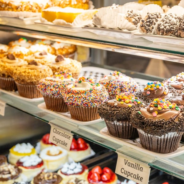 A deli display case filled with various cupcakes, including chocolate, vanilla, and sprinkle-covered.