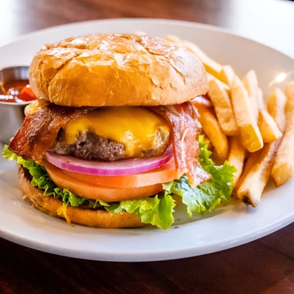 A Pickles Deli bacon cheeseburger with lettuce, tomato, and onion, served with fries and ketchup.