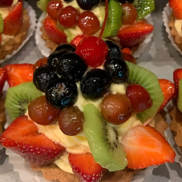 Close-up of a fruit tart with strawberries, kiwi, grapes, blueberries, and a cherry on top.