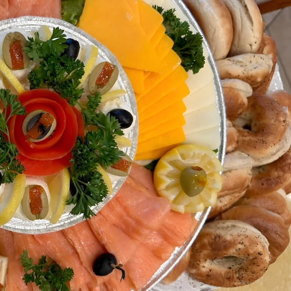 A deli platter with smoked salmon, sliced cheese, bagels, olives, lemons, and parsley.